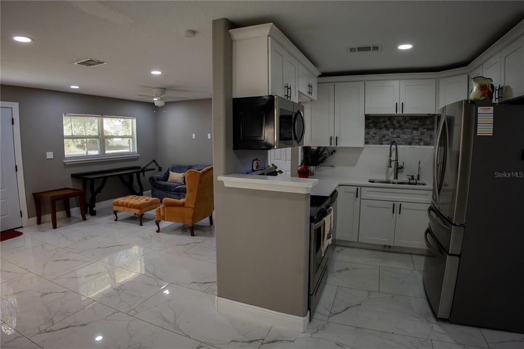 A kitchen with white cabinets and a stainless steel refrigerator opens to a living area — 1741 S HAWTHORNE AVENUE, APOPKA, FL