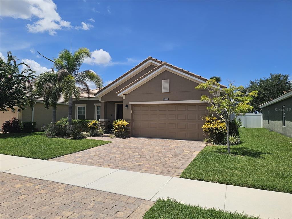 A single-story house with a tan stucco exterior, a two-car garage, and a paved driveway — 11680 SW ROWENA STREET, PORT ST LUCIE, FL