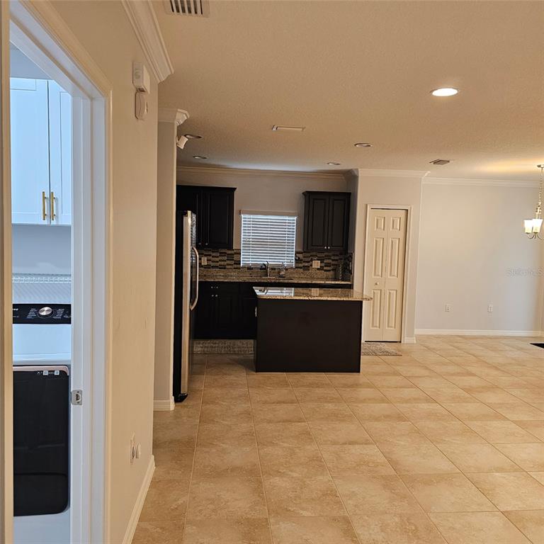 A kitchen with dark cabinets and a granite island opens into a tiled living area — 11680 SW ROWENA STREET, PORT ST LUCIE, FL