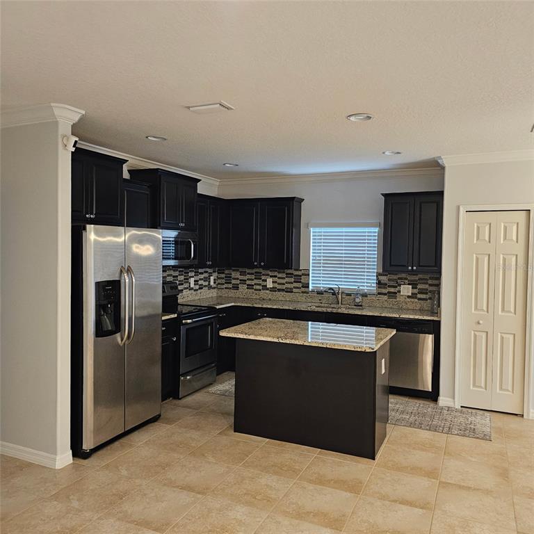 A kitchen features dark cabinets, granite countertops, stainless steel appliances, and a central island — 11680 SW ROWENA STREET, PORT ST LUCIE, FL