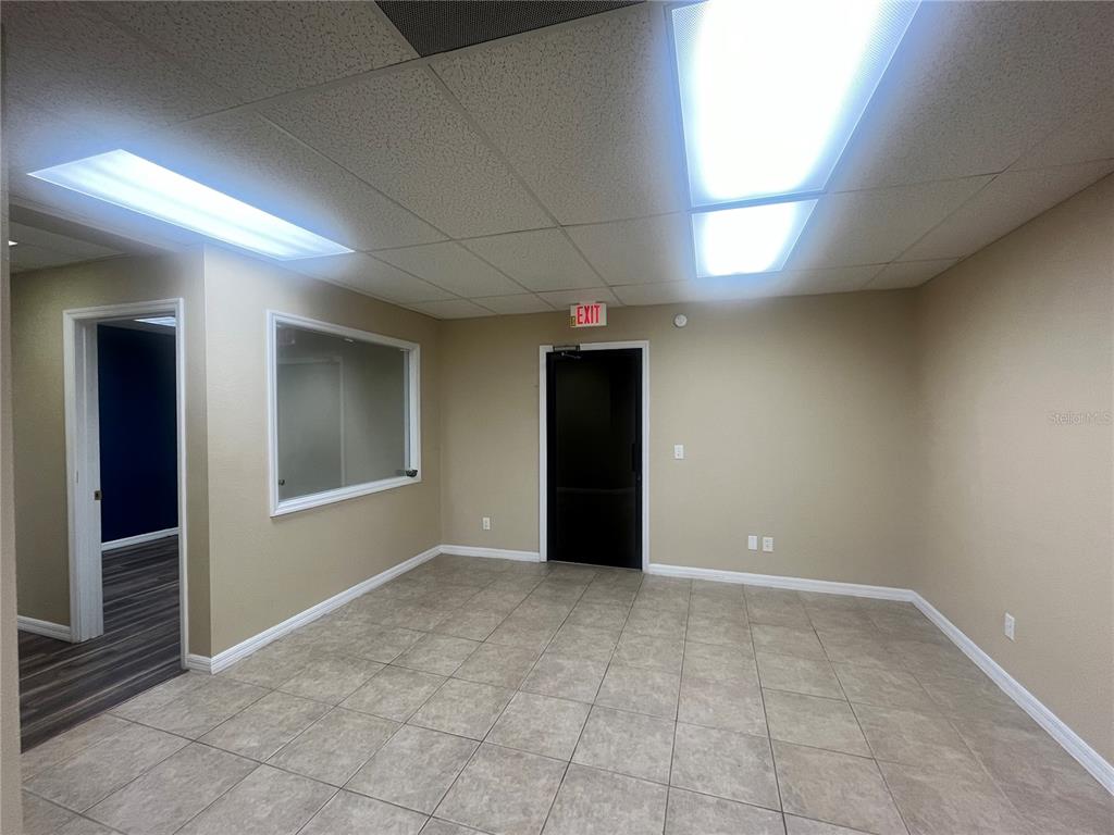 An empty office space features beige walls, tile flooring, a black door, and fluorescent lighting — 141 E CENTRAL AVENUE UNIT 350, WINTER HAVEN, FL