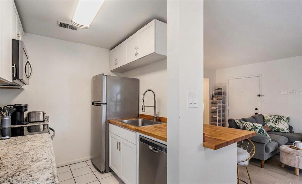 A kitchen with white cabinets, stainless steel appliances, and wood countertops opens to a living area — 2109 W DE LEON STREET, TAMPA, FL