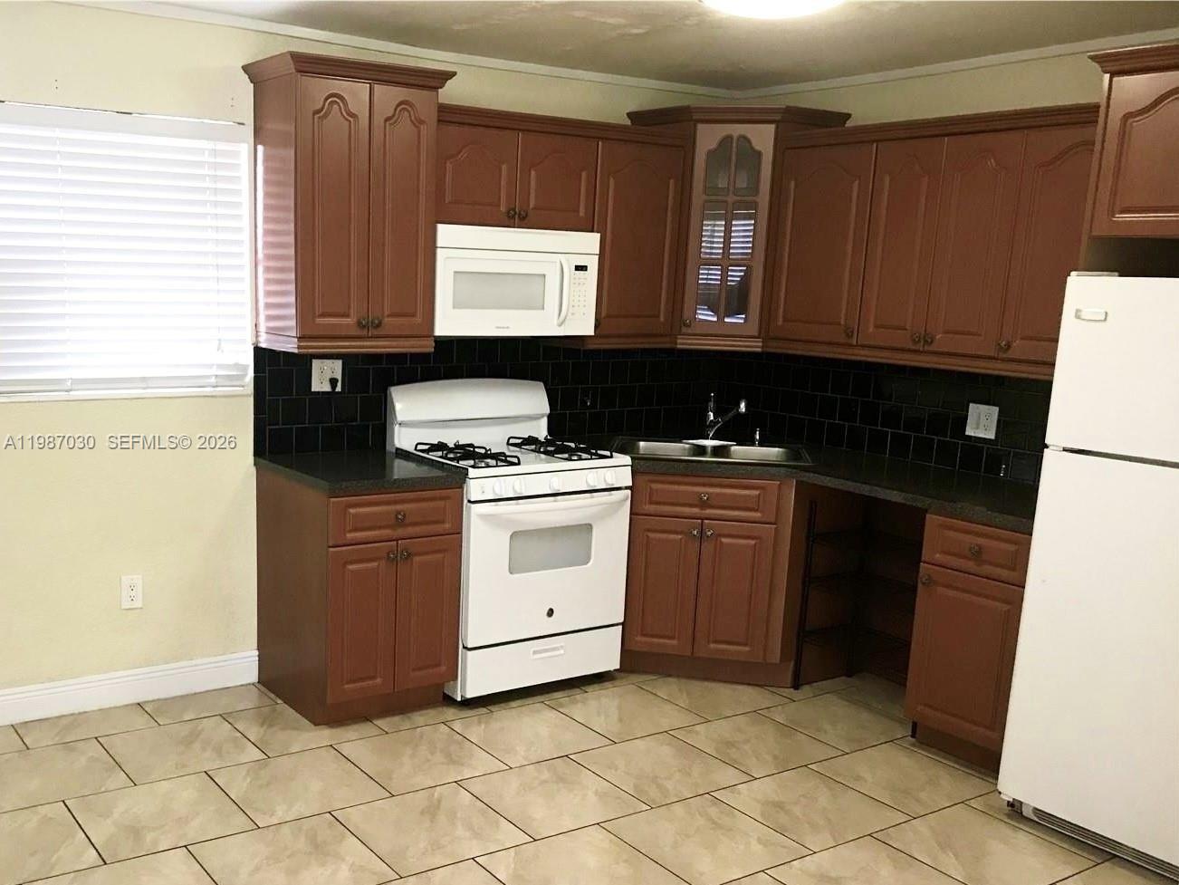 A kitchen features brown wooden cabinets, a white stove, a microwave, and black tile backsplashes — 4250 SW 67th Ave # 32, Miami FL 33155, MIAMI, FL