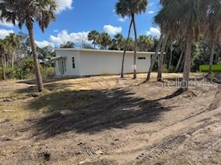 A white, single-story house sits on a cleared, dirt lot surrounded by palm trees — 16411 BAUERS AVENUE, PORT CHARLOTTE, FL