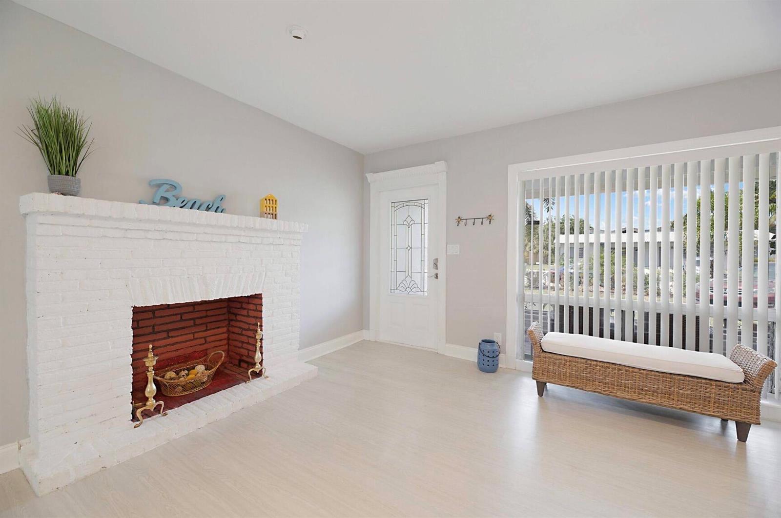 A living room features a white brick fireplace, light wood flooring, and a wicker bench — 2740 SE 1st Court, Pompano Beach FL 33062, POMPANO BEACH, FL