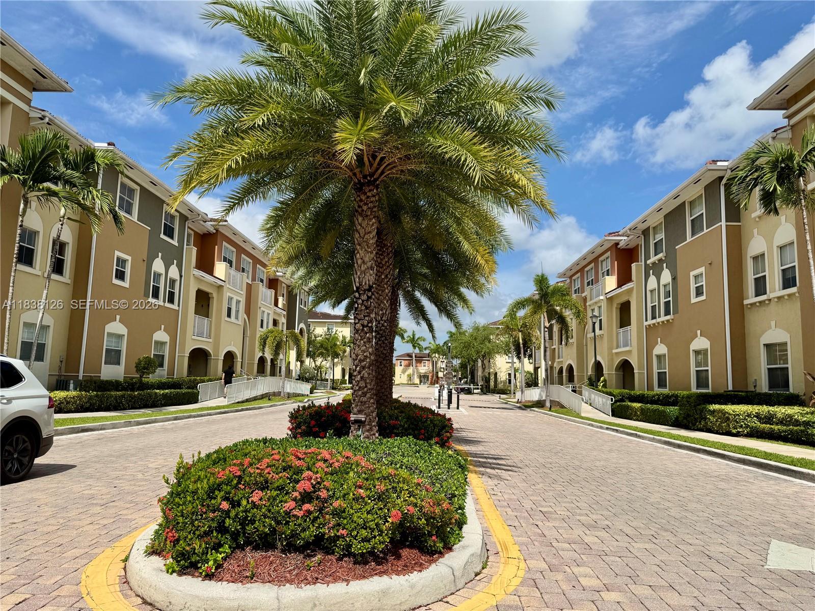 A paved driveway leads between two multi-story apartment buildings with palm trees and landscaping — 8800 NW 107th Ct # 202, Doral FL 33178, DORAL, FL
