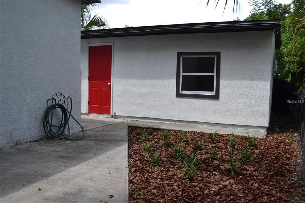 A white exterior building features a red door, a single window, and a concrete walkway — 8210 N KLONDYKE STREET, TAMPA, FL