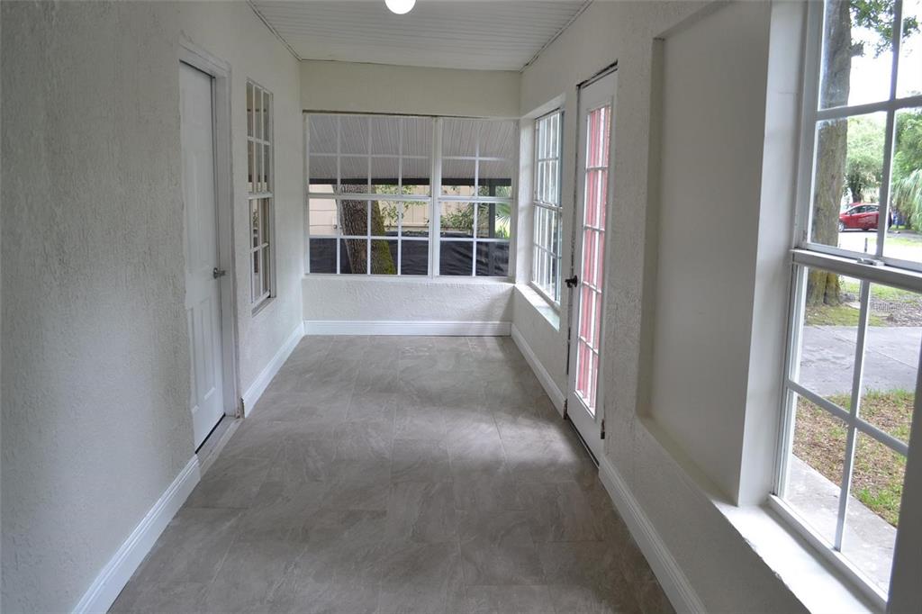 A sunroom with gray tile flooring, white walls, and multiple windows looking out to greenery — 8210 N KLONDYKE STREET, TAMPA, FL