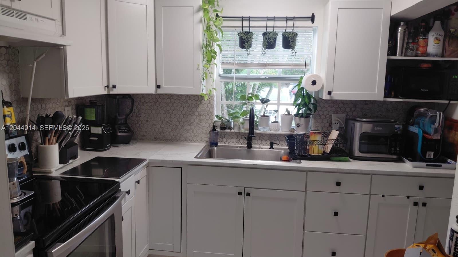 A kitchen features white cabinets, a hexagon tile backsplash, and a window above the sink — 6461 Miramar Pkwy, Miramar FL 33023, MIRAMAR, FL