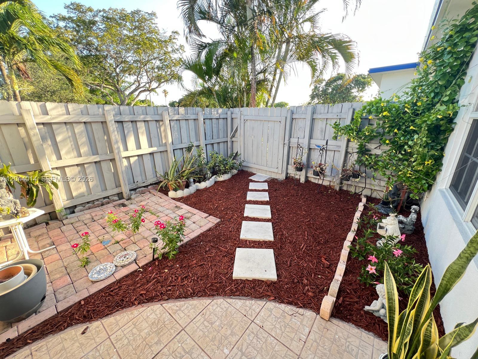A fenced backyard features a brick patio, a mulch area with stone pavers, and landscaping — 6461 Miramar Pkwy, Miramar FL 33023, MIRAMAR, FL