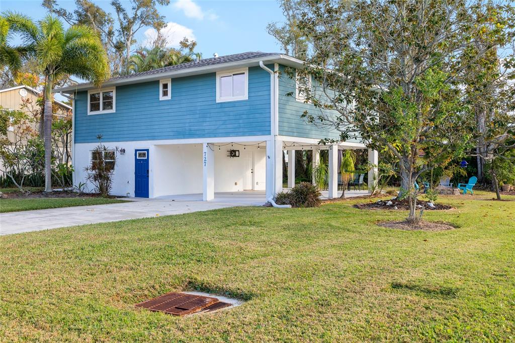 A two-story house with blue siding, a white ground-level carport, and a lawn with a drain — 727 47TH STREET W, PALMETTO, FL