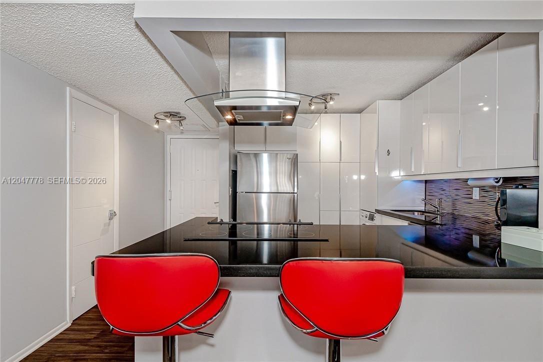 A modern kitchen features white cabinets, a black countertop, and two red bar stools — 200 Leslie Dr # 926, Hallandale Beach FL 33009, HALLANDALE BEACH, FL