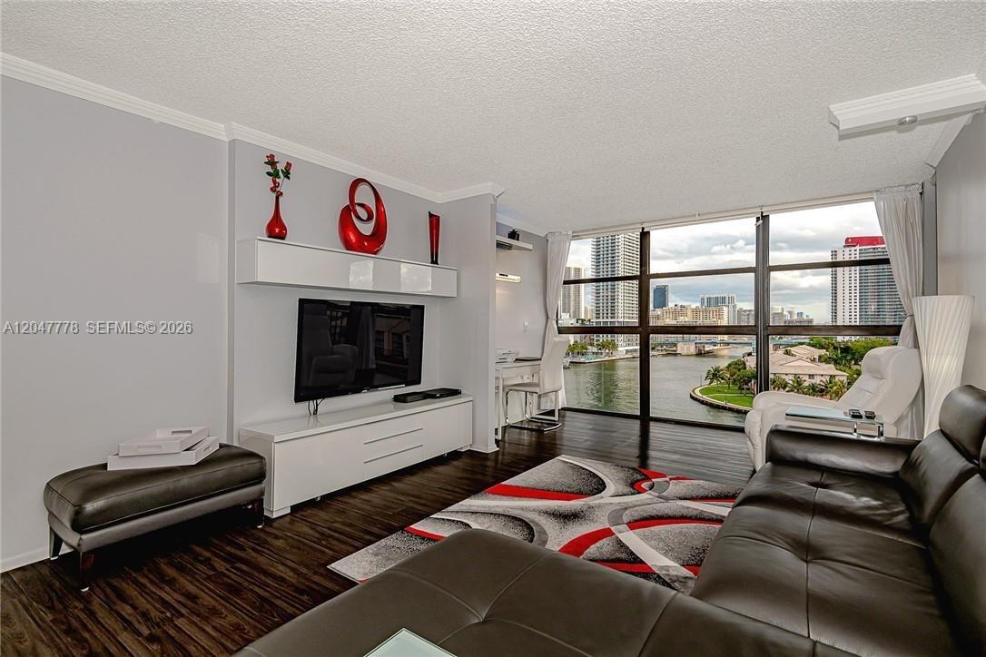 A living room features a dark leather sofa, a wall-mounted television, and floor-to-ceiling windows — 200 Leslie Dr # 926, Hallandale Beach FL 33009, HALLANDALE BEACH, FL