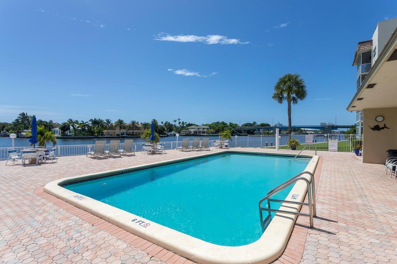 A swimming pool with a paved deck overlooks a canal with a bridge in the distance — 650 Snug Harbor Drive # G301, Boynton Beach FL 33435, BOYNTON BEACH, FL