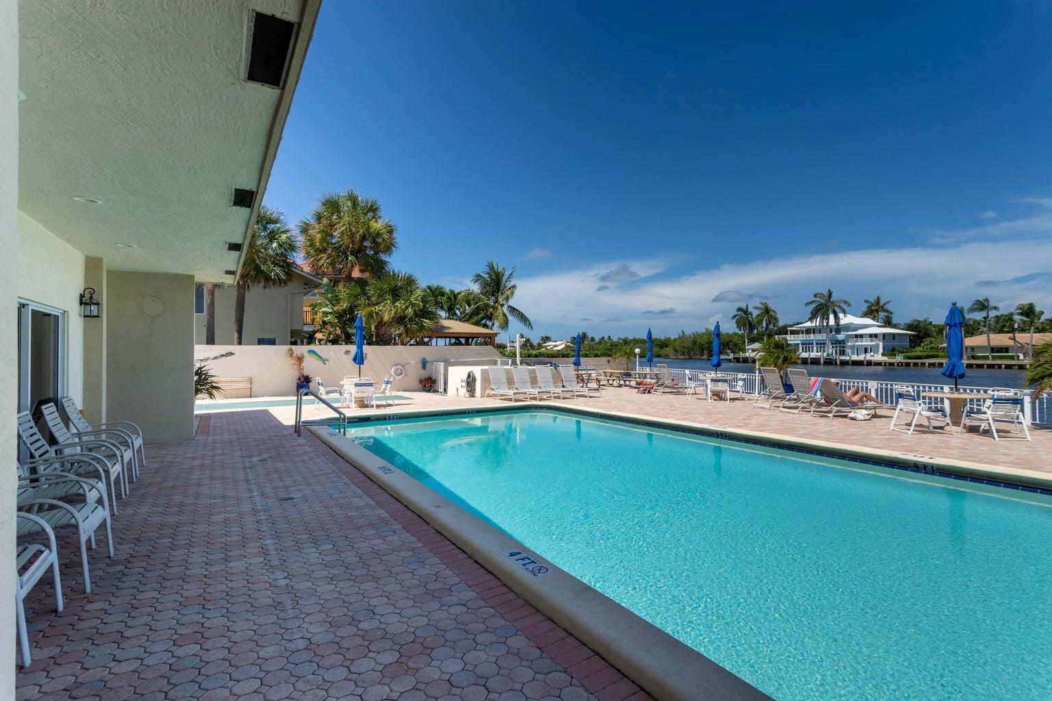 A swimming pool sits on a paved patio next to a building overlooking a canal — 650 Snug Harbor Drive # G301, Boynton Beach FL 33435, BOYNTON BEACH, FL