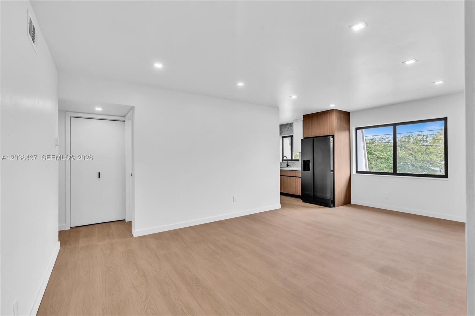 A bright, open-concept living area features light wood-look flooring and a modern kitchen beyond — 1924 NE 26th St # 4, Wilton Manors FL 33305, WILTON MANORS, FL
