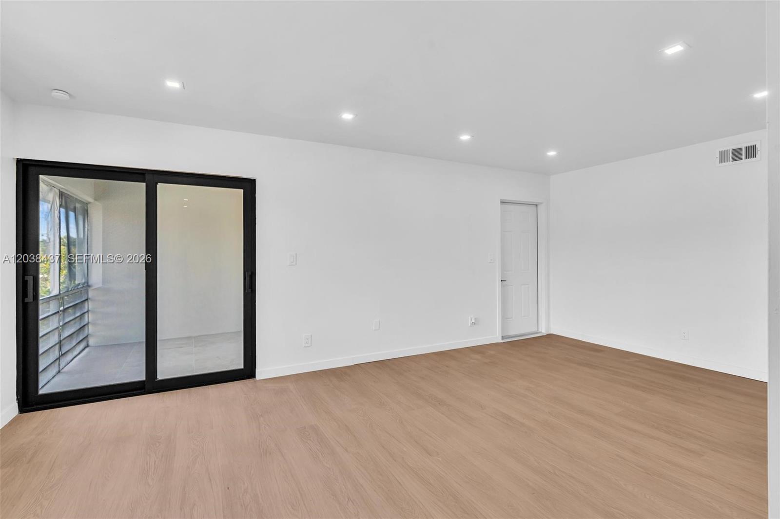 An empty room features light wood-look flooring, white walls, recessed lighting, and a sliding glass door — 1924 NE 26th St # 4, Wilton Manors FL 33305, WILTON MANORS, FL