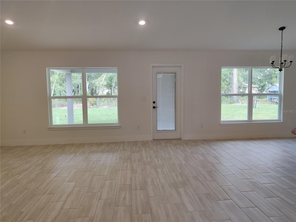 A bright, empty room features light wood-look tile flooring, two windows, and a glass-paneled door — 14606 MOCKING WREN ROAD, WEEKI WACHEE, FL