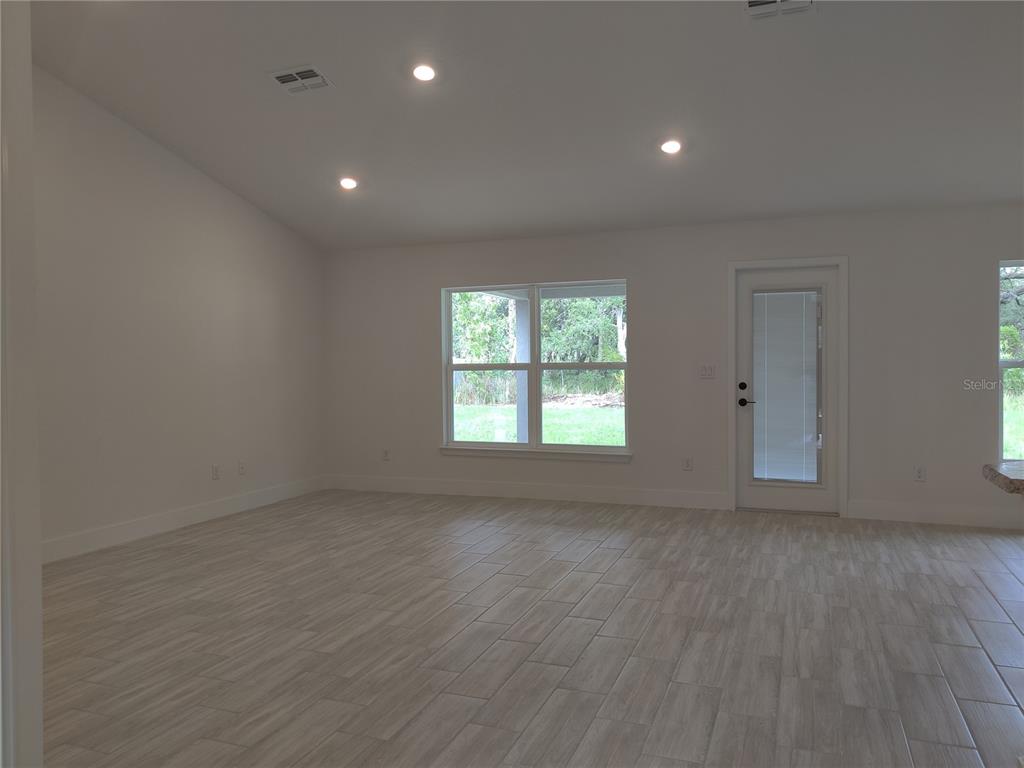 A bright, empty room features light-colored wood-look tile flooring, white walls, recessed lighting, and a glass-paneled door — 14606 MOCKING WREN ROAD, WEEKI WACHEE, FL