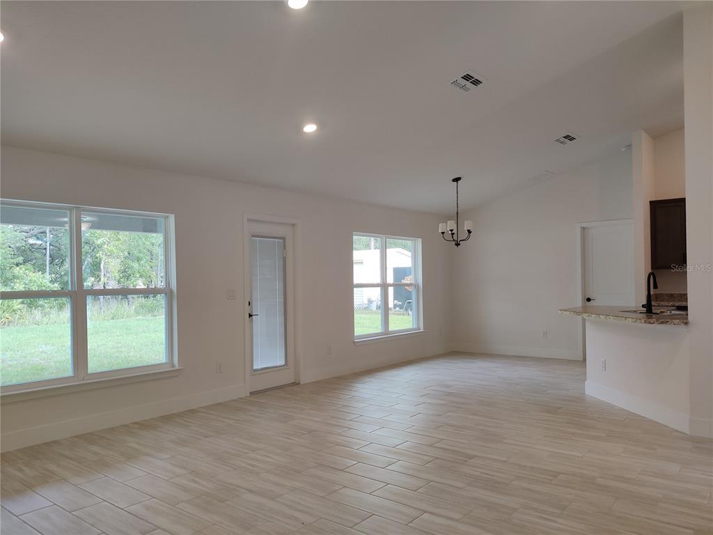 An open-concept room features light wood-look tile flooring, white walls, and a kitchen breakfast bar — 14606 MOCKING WREN ROAD, WEEKI WACHEE, FL