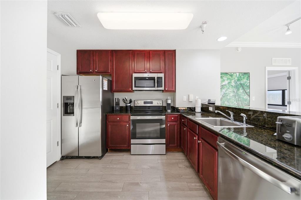 A kitchen features dark wood cabinets, granite countertops, and stainless steel appliances on wood-look flooring — 14051 GROVE RESORT AVENUE UNIT 1705, WINTER GARDEN, FL
