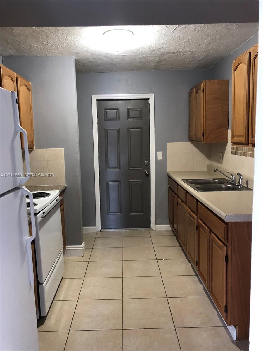 A galley kitchen features wood cabinets, light countertops, tile flooring, and a dark exterior door — 424 SW 12th Ave, Homestead FL 33030, HOMESTEAD, FL