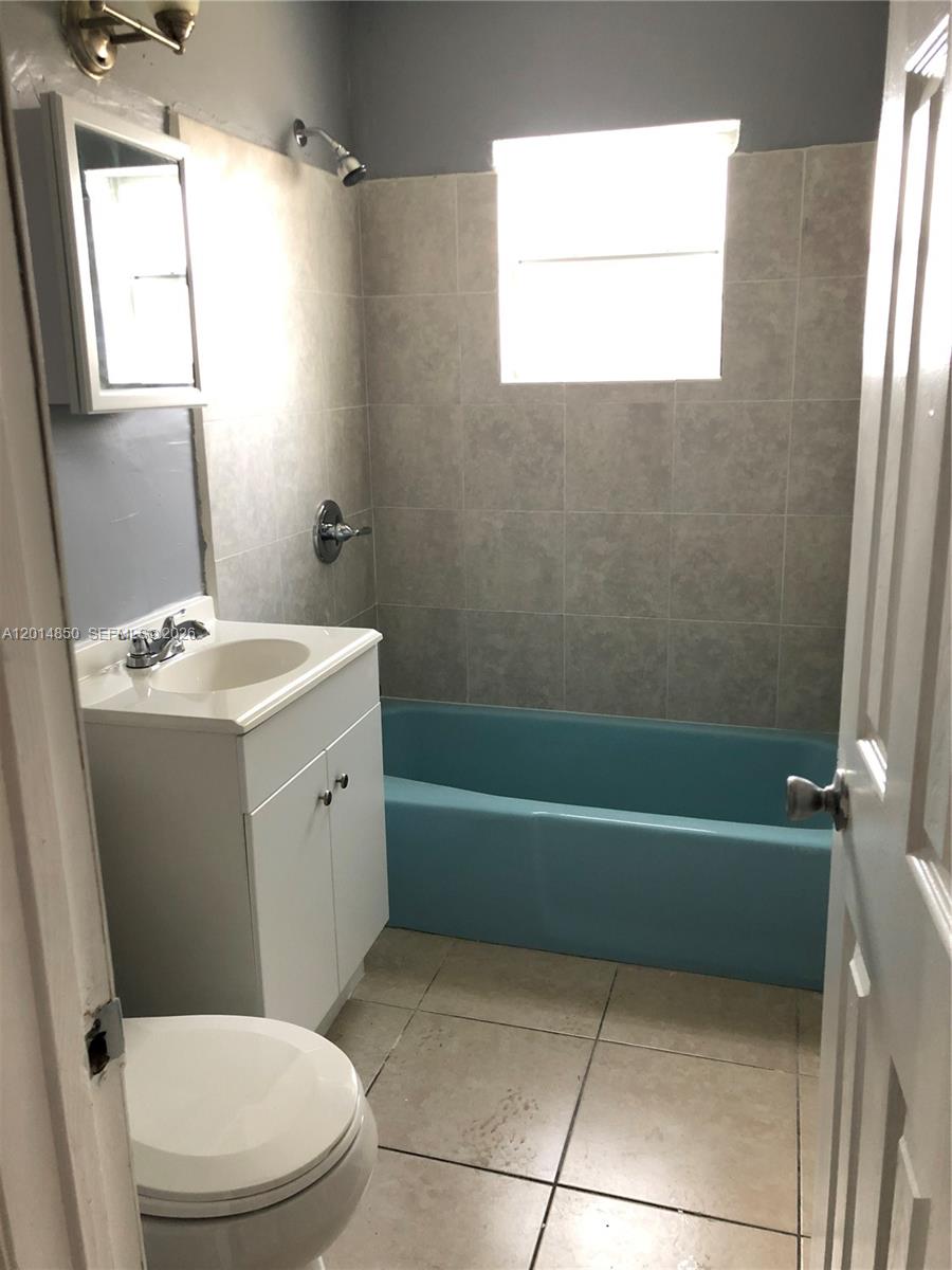 A bathroom features a blue bathtub, a white vanity, a toilet, and light-colored tiled walls — 424 SW 12th Ave, Homestead FL 33030, HOMESTEAD, FL