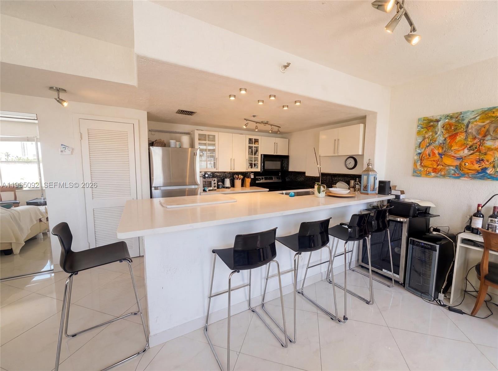 A kitchen features white cabinetry, a long breakfast bar with black stools, and tile flooring — 802 Euclid Ave # 305, Miami Beach FL 33139, MIAMI BEACH, FL