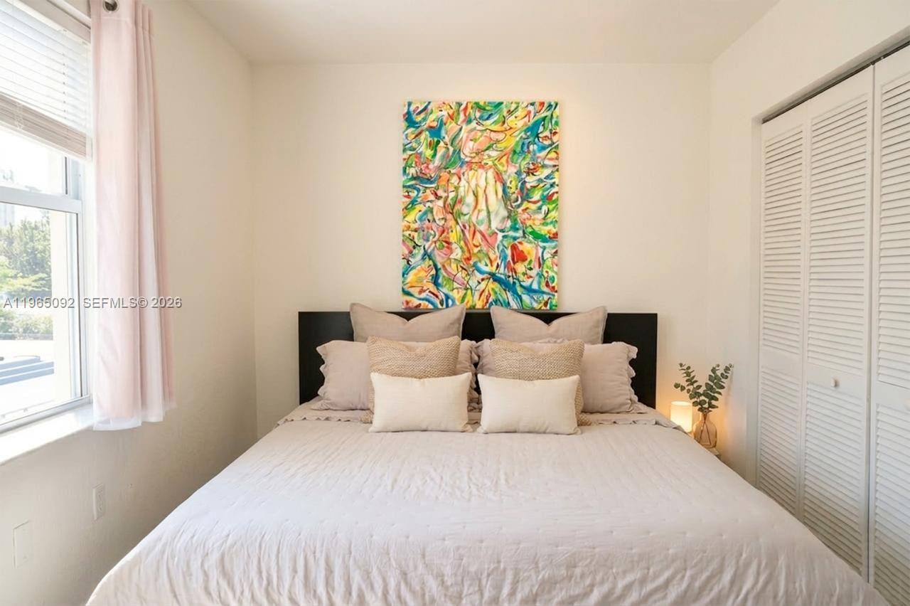 A bedroom features a bed with neutral bedding, a colorful abstract painting, and white shutters — 802 Euclid Ave # 305, Miami Beach FL 33139, MIAMI BEACH, FL