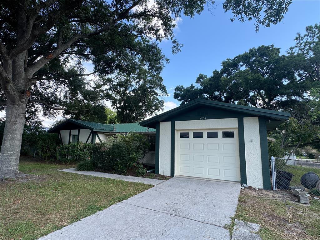 A single-story house with a white garage door, dark green trim, and mature trees — 624 WOOD ROAD, SEFFNER, FL