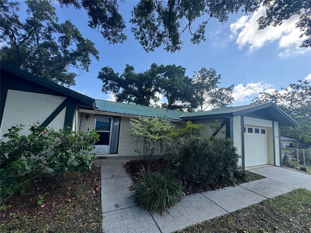 A single-story house with a green metal roof, white brick siding, and an attached garage — 624 WOOD ROAD, SEFFNER, FL