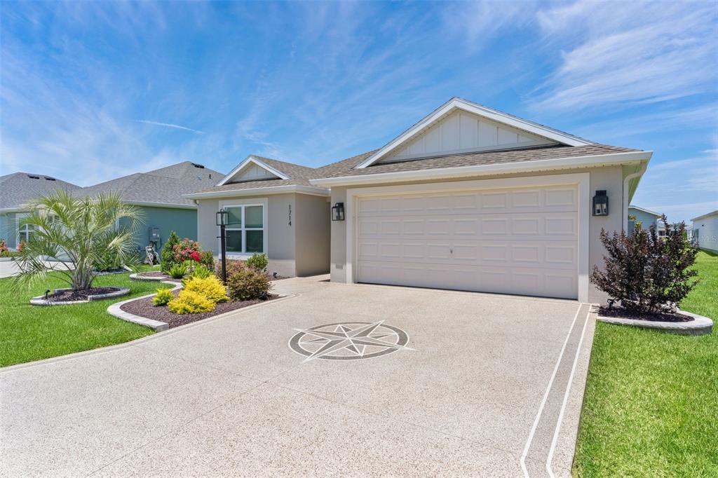 A single-story house with a beige exterior, a two-car garage, and a decorative compass driveway — 1714 MCMURTRIE LOOP, THE VILLAGES, FL