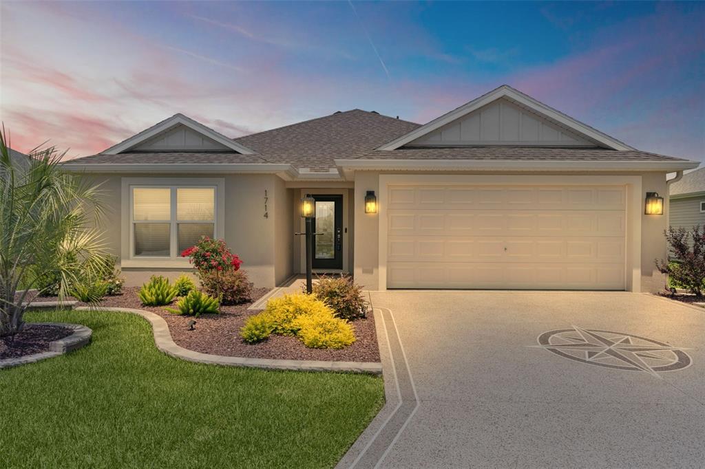 A single-story suburban house features a beige stucco exterior, a two-car garage, and landscaping — 1714 MCMURTRIE LOOP, THE VILLAGES, FL