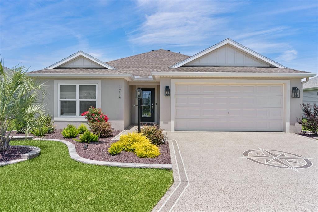 A single-story house with a beige stucco exterior, a two-car garage, and a landscaped yard — 1714 MCMURTRIE LOOP, THE VILLAGES, FL