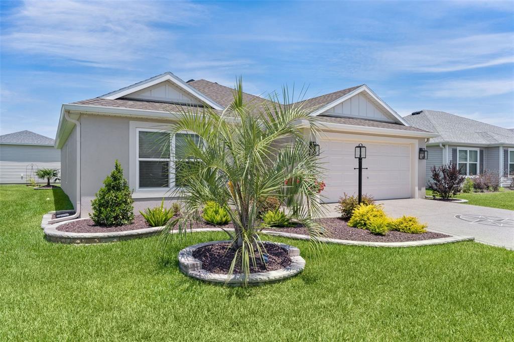 A single-story house with a beige stucco exterior, a two-car garage, and landscaped front yard — 1714 MCMURTRIE LOOP, THE VILLAGES, FL