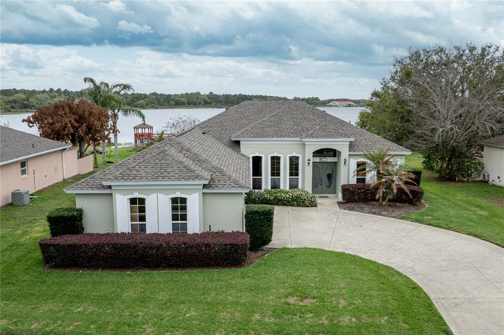 A single-story house with a concrete driveway, green lawn, and a lake in the background — 3804 BAYSHORE CIRCLE, TAVARES, FL