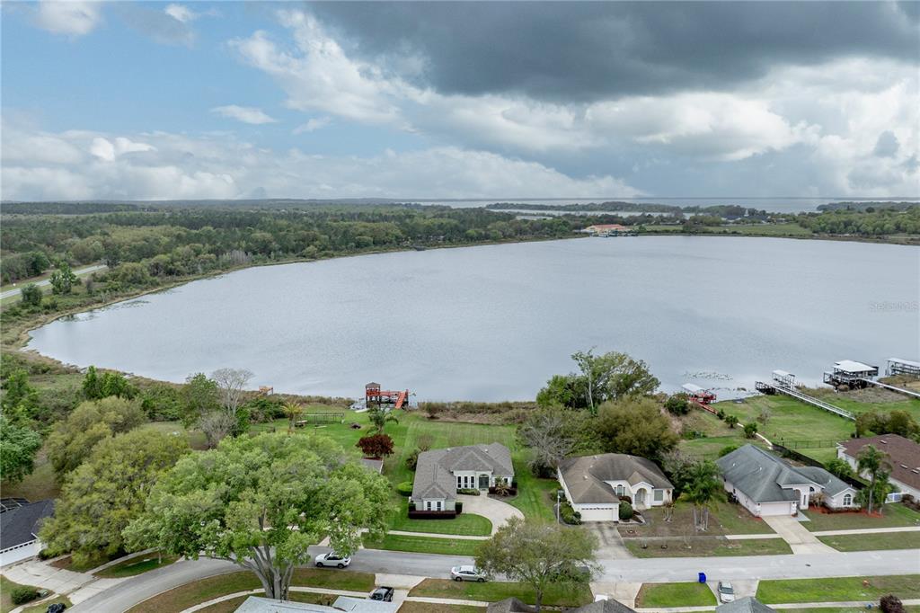An aerial view shows several houses along a lakefront with docks and a cloudy sky — 3804 BAYSHORE CIRCLE, TAVARES, FL