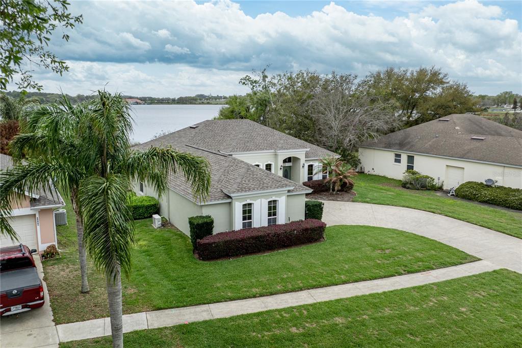 An aerial view of a single-story house with a driveway, lawn, and lakefront backyard — 3804 BAYSHORE CIRCLE, TAVARES, FL