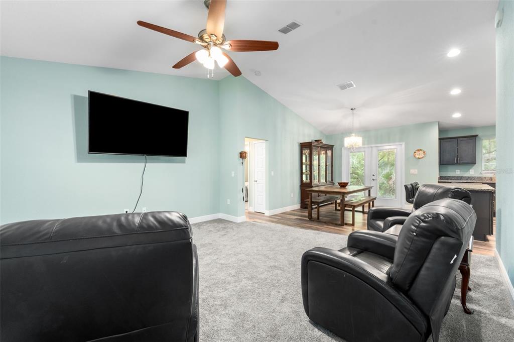 A living room with light blue walls, gray carpeting, black leather furniture, and a ceiling fan — 6144 AVENUE G, MC INTOSH, FL