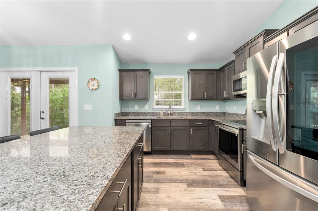 A kitchen features dark wood cabinets, granite countertops, stainless steel appliances, and light blue walls — 6144 AVENUE G, MC INTOSH, FL