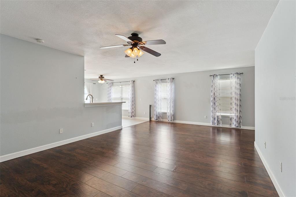 A spacious living room with dark wood-look flooring, light gray walls, and a ceiling fan — 825 CLIFTON HILLS STREET, ORLANDO, FL