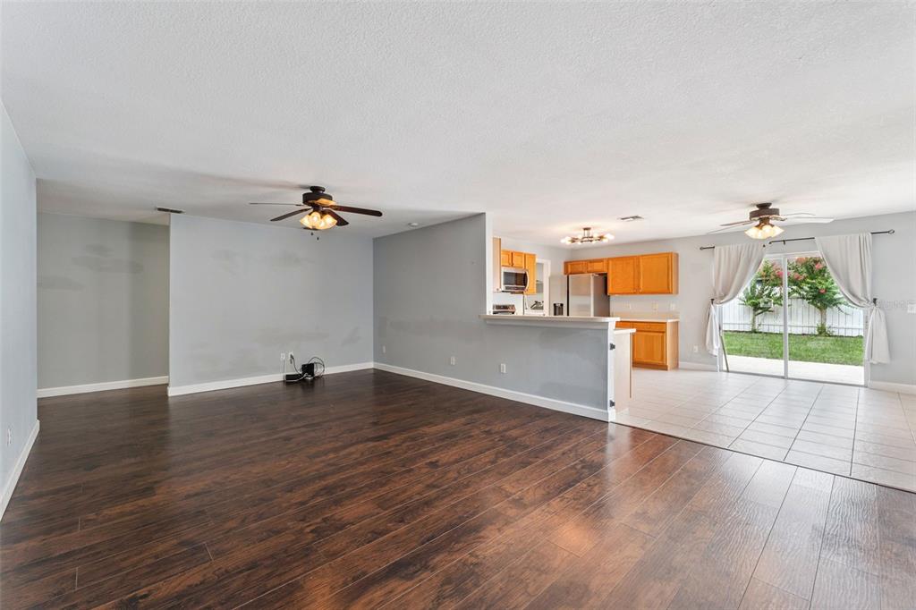 An open-concept living room with dark wood flooring flows into a tiled kitchen and patio — 825 CLIFTON HILLS STREET, ORLANDO, FL
