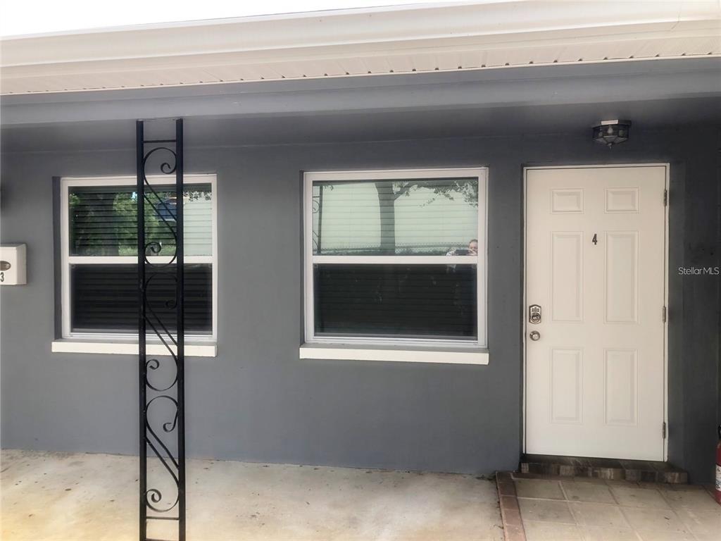 The exterior of a gray building features two windows, a white front door, and a metal post — 520 70TH STREET N UNIT 4, ST PETERSBURG, FL