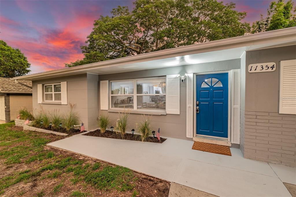 A single-story gray house with a blue front door and white shutters sits at dusk — 11354 123RD TERRACE N, LARGO, FL