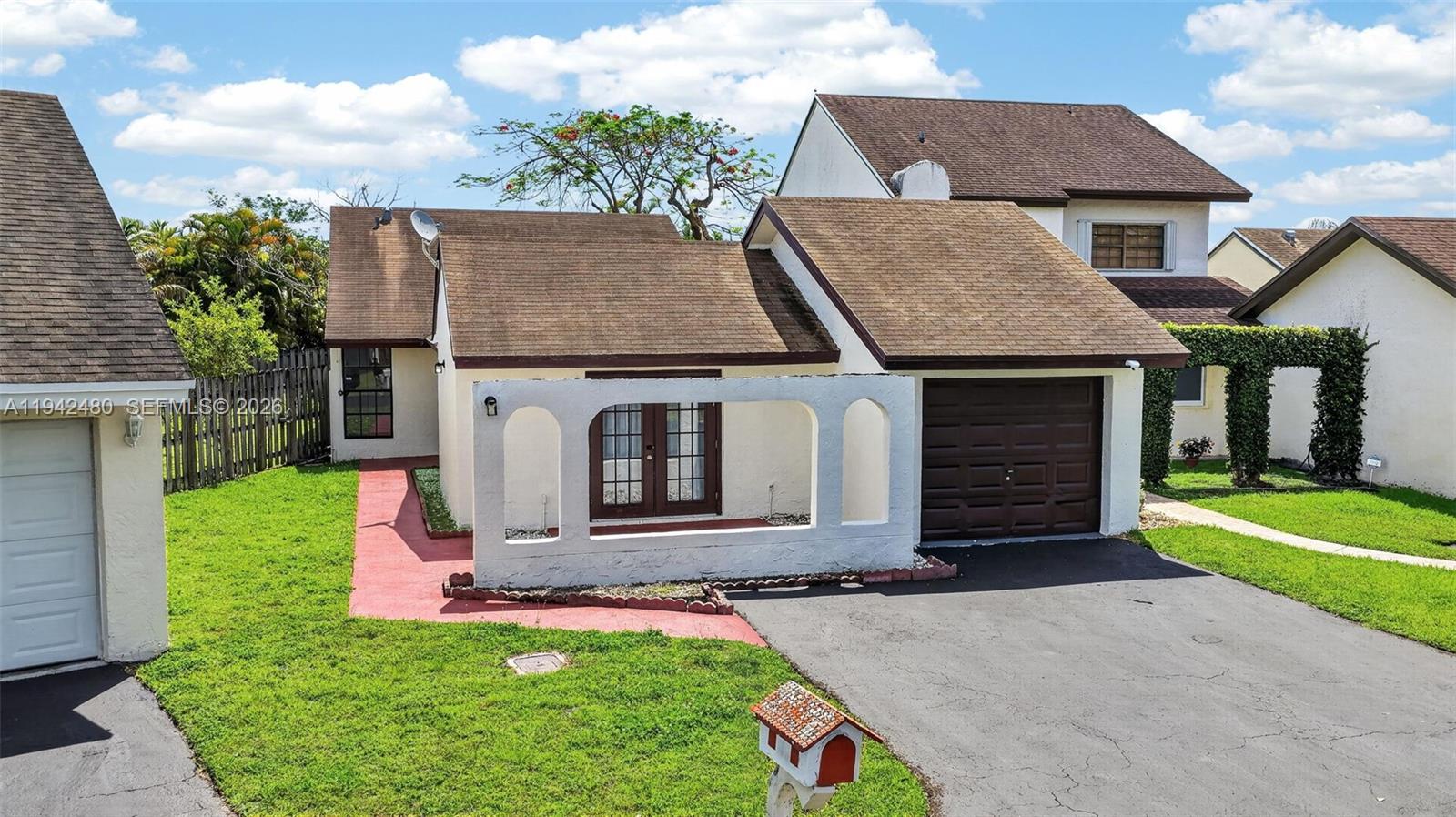 A single-story house features a white arched privacy wall, a brown garage door, and a driveway — 6905 SW 104th Ct, Miami FL 33173, MIAMI, FL