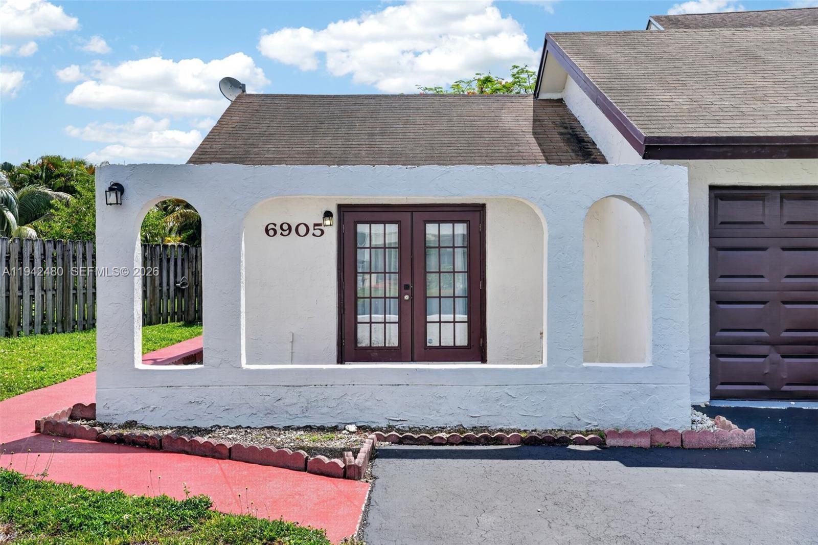The exterior of a house features a white stucco facade with arched openings and double doors — 6905 SW 104th Ct, Miami FL 33173, MIAMI, FL