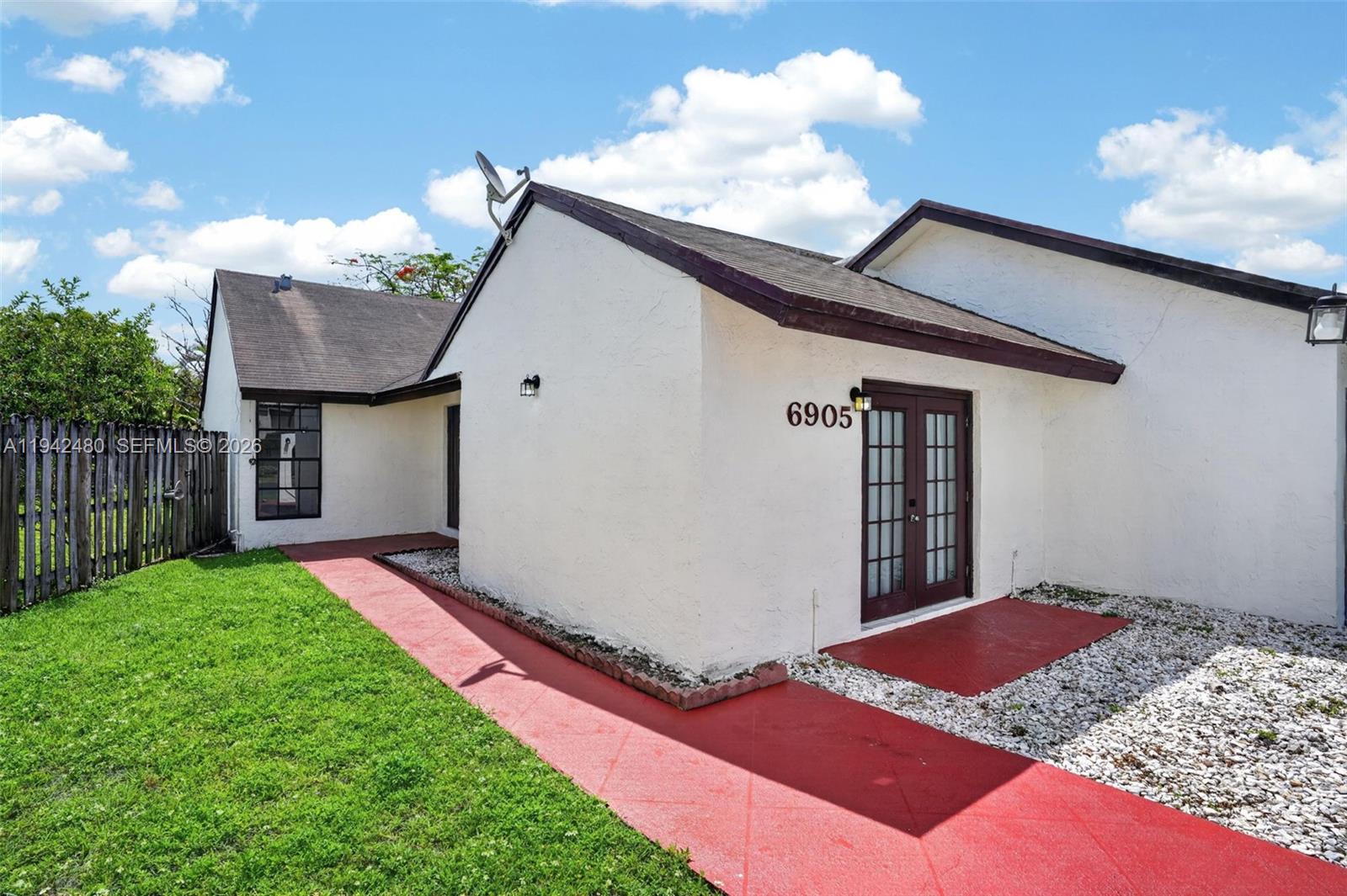 A white stucco house exterior features a red painted walkway and dark French doors — 6905 SW 104th Ct, Miami FL 33173, MIAMI, FL