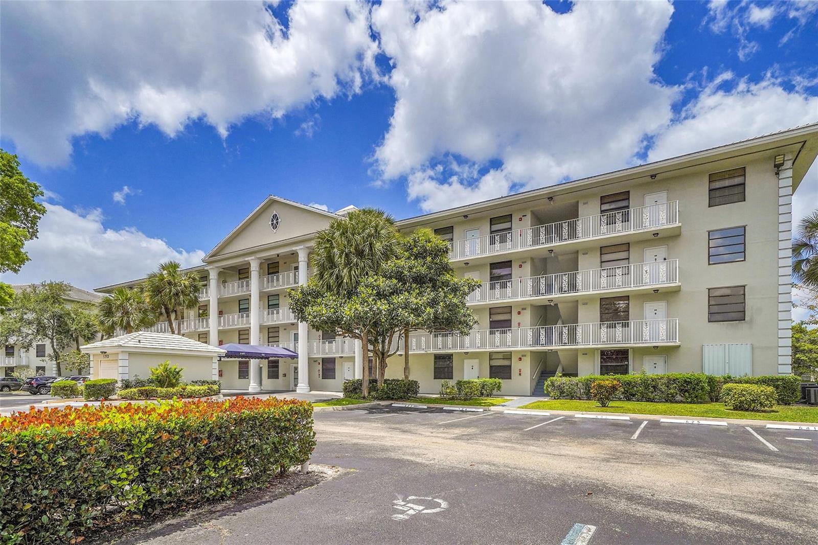 A multi-story apartment building with a white facade, columns, and balconies sits by a parking lot — 1713 Whitehall Drive # 103, Davie FL 33324, DAVIE, FL