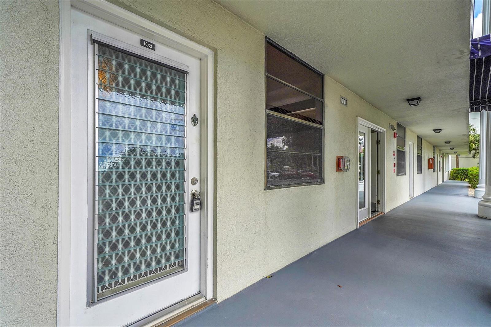 A white door with a decorative glass insert and a lockbox opens onto a covered walkway — 1713 Whitehall Drive # 103, Davie FL 33324, DAVIE, FL