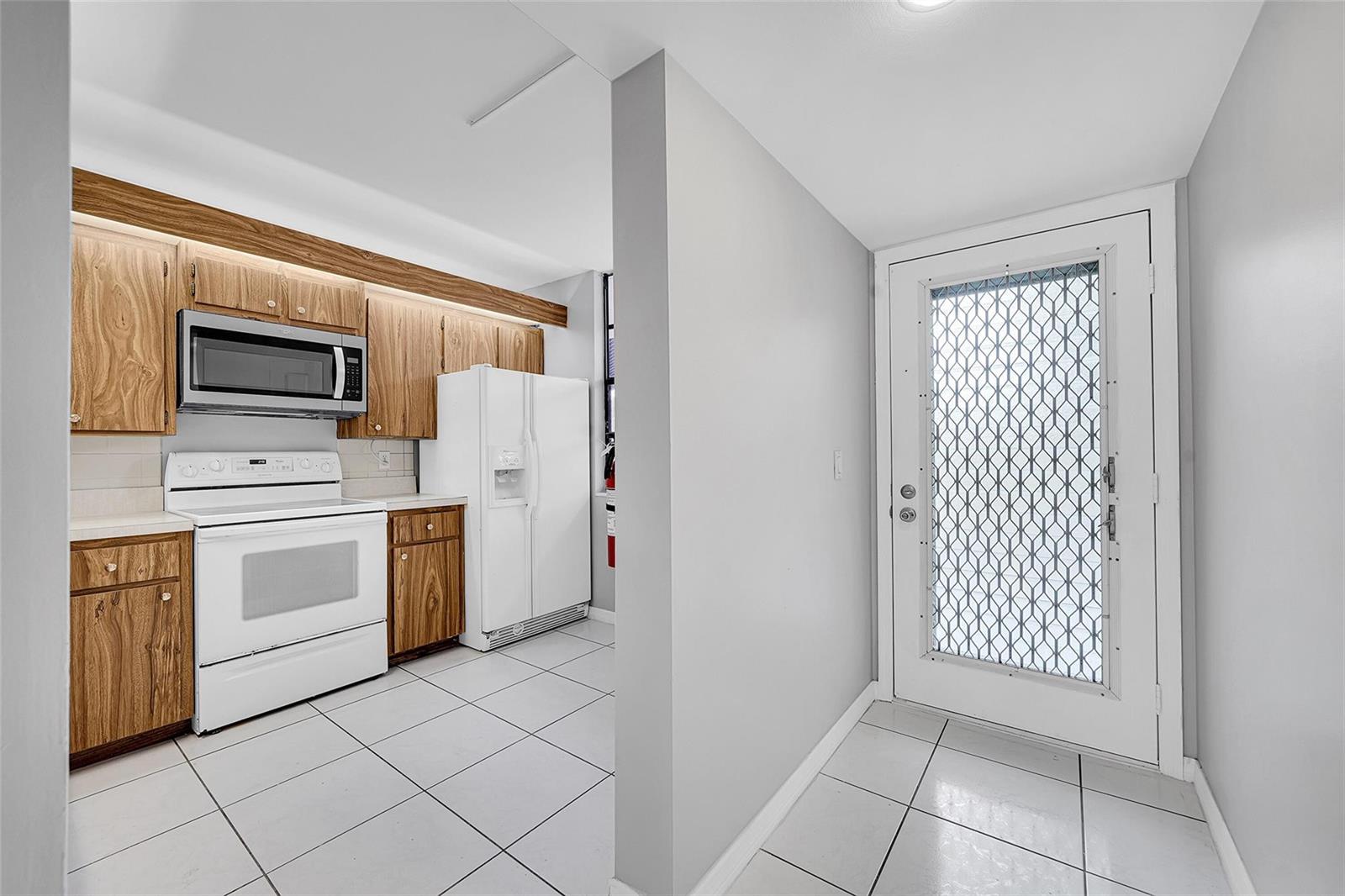 A kitchen with wood cabinets, white appliances, and tile flooring next to a glass-paned door — 1713 Whitehall Drive # 103, Davie FL 33324, DAVIE, FL